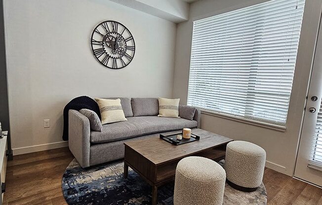 A living room with a grey couch, a coffee table, and a clock on the wall.