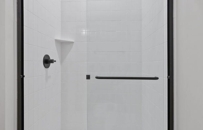 A white tiled shower with a black frame and a black handle.