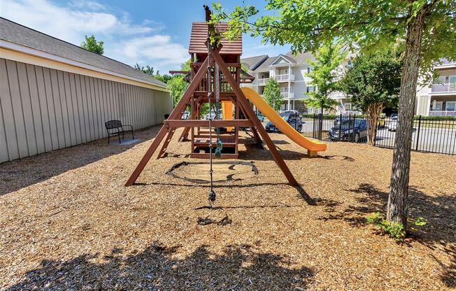 Rope hanging from the playground on a floor of wood chips  near a bench, street parking, and trees