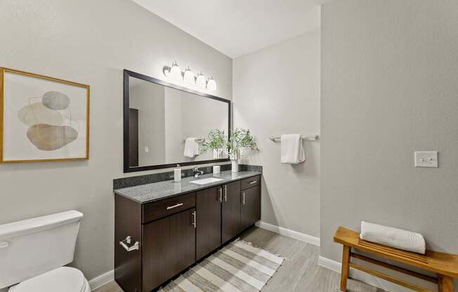 A bathroom with a white toilet, a wooden bench, and a large mirror.