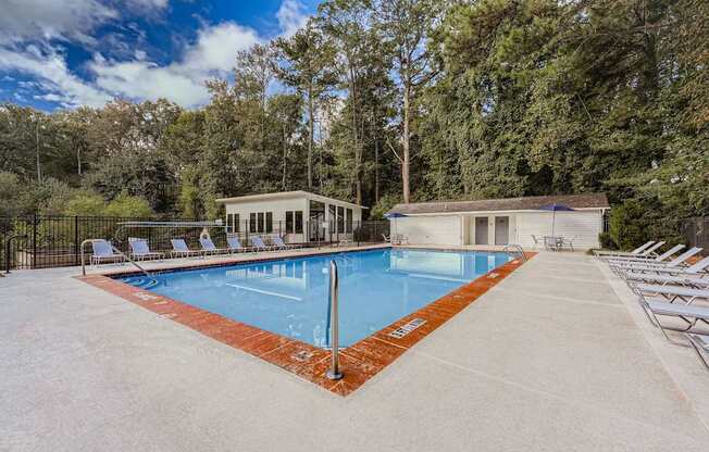 A large outdoor swimming pool surrounded by trees and lounge chairs.