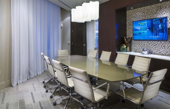 Conference table with 8 rolling leather chairs in a room with wood-paneled walls, floor-to-ceiling windows, and a wall-mounted HDTV.