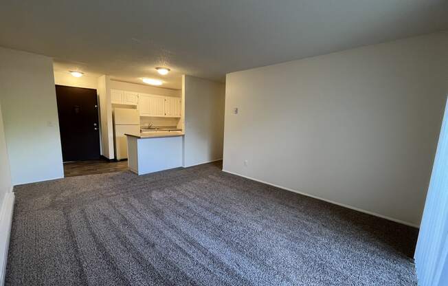 an empty living room with a kitchen in the background