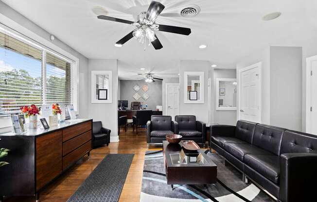 A black leather couch sits in a well-lit living room with a ceiling fan overhead.
