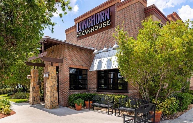 the exterior of the longhorn steakhouse with benches and trees
