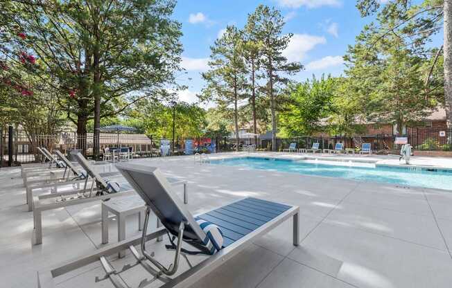 A pool area with sun loungers and trees.
