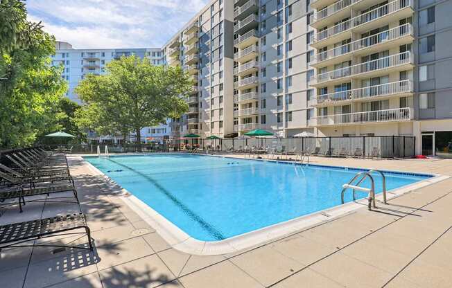 A large swimming pool surrounded by lounge chairs and umbrellas in a residential area.