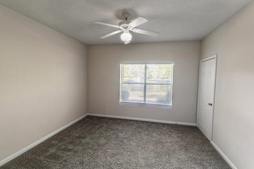 an empty bedroom with a ceiling fan and a window