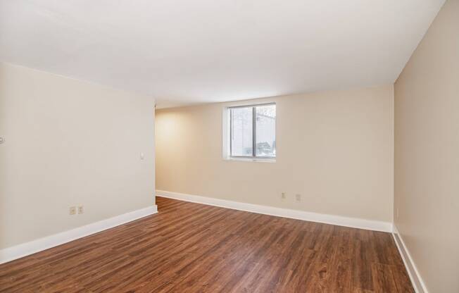 an empty living room with wood flooring and a window