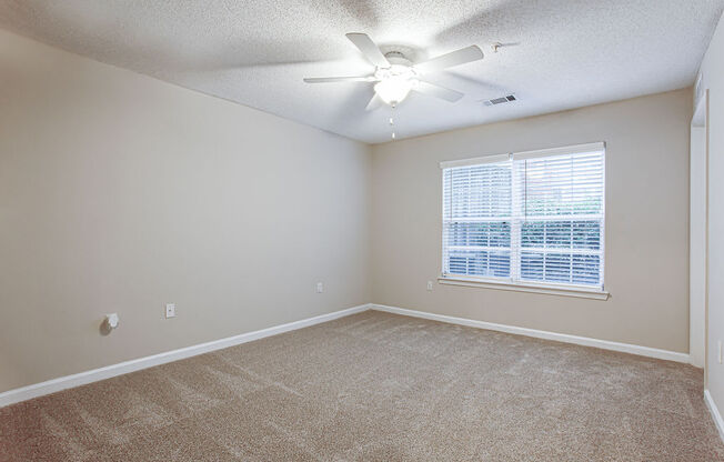 an empty living room with a large window and a ceiling fan