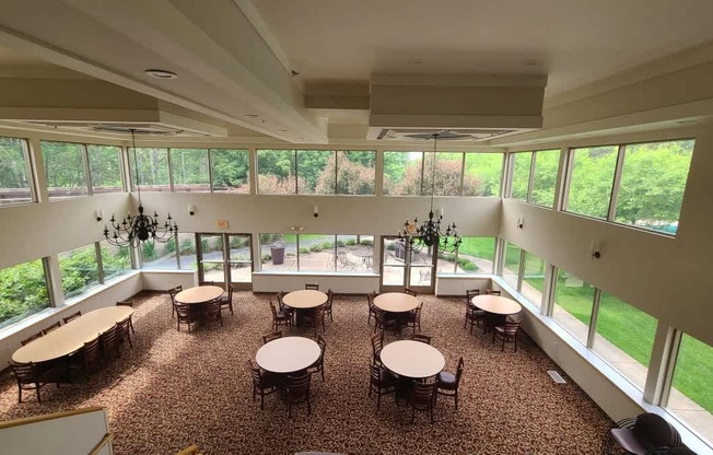 A large room with tables and chairs and windows overlooking a green lawn.