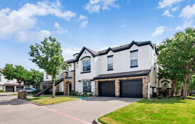 Apartment building exterior with attached garages, exterior staircase, and manicured lawn.