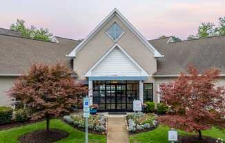 The leasing office with a white roof and a glass door is surrounded by trees and bushes.