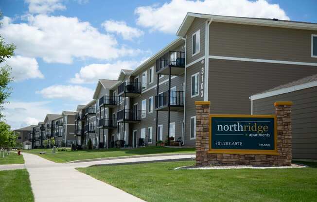 Outside view of Northridge Apartments and the large brick lined sign. Building is gray with white trim and balconies are present on every floor.