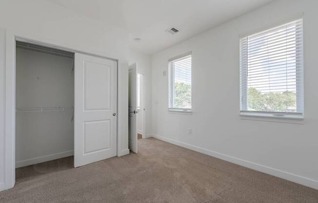 A room with a carpeted floor, a window with blinds, and a door leading to another room.