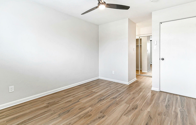 Bright and airy bedroom with sleek wood flooring, ceiling fan, and spacious closet for modern living.