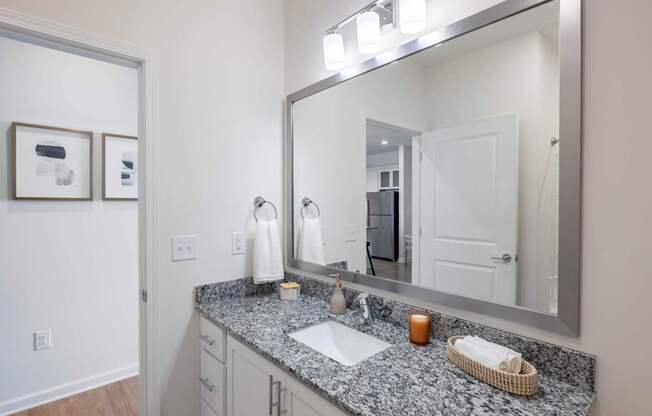A bathroom with a granite countertop and a large mirror.at Evolve at Parkway Apartment Homes, Concord, 28027