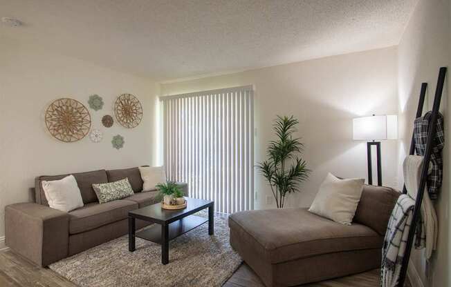 Living room with a couch, chaise lounge and a potted plant in a 515 square foot 1 bedroom, 1 bath apartment home at Canyon Creek Apartments in Dallas Midtown neighborhood of Dallas, TX.