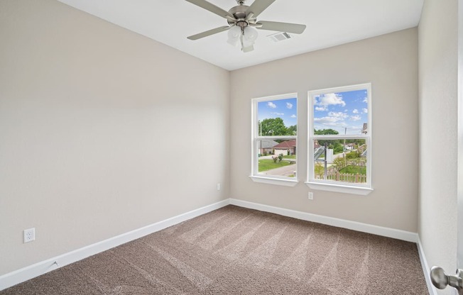 A room with a ceiling fan and two windows.