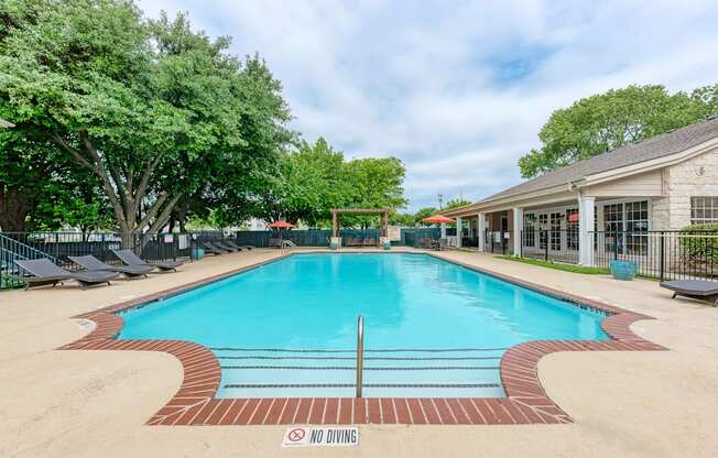A large outdoor swimming pool surrounded by trees and lounge chairs.