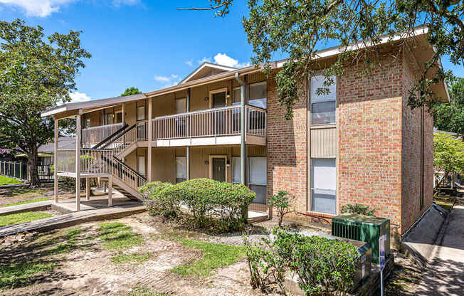 A two-story brick apartment building with a balcony and a small garden in front.