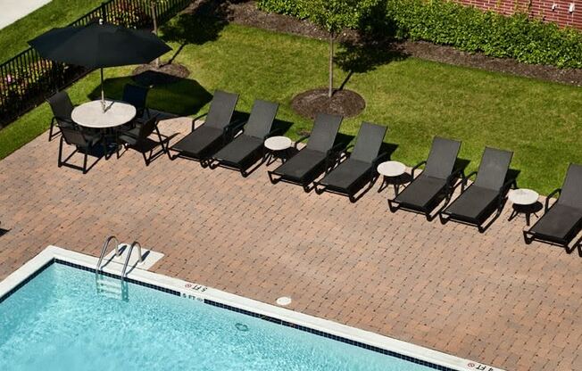 an aerial view of a pool and patio with black lounge chairs and umbrellas  at The Sheffield Englewood, Englewood