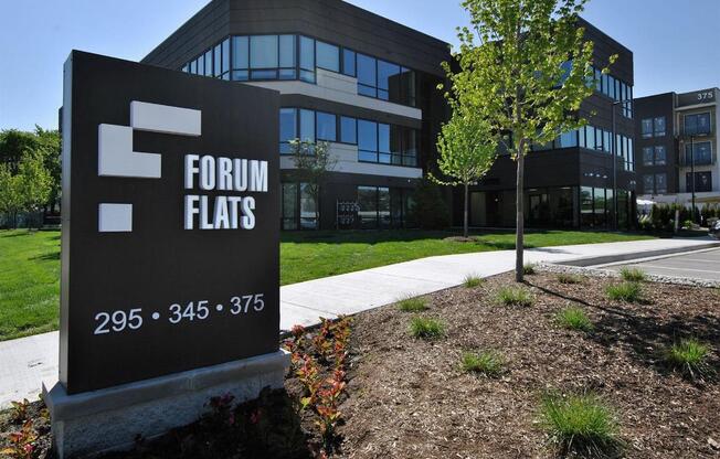 A sign for Forum Flats stands in front of a modern building.