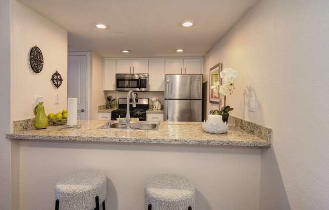 Kitchen Bar Seating with White Bar Stools, Granite Countertop, Sink, Refrigerator and Microwave