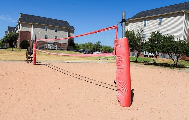 a red net on a sandy playground with houses in the background