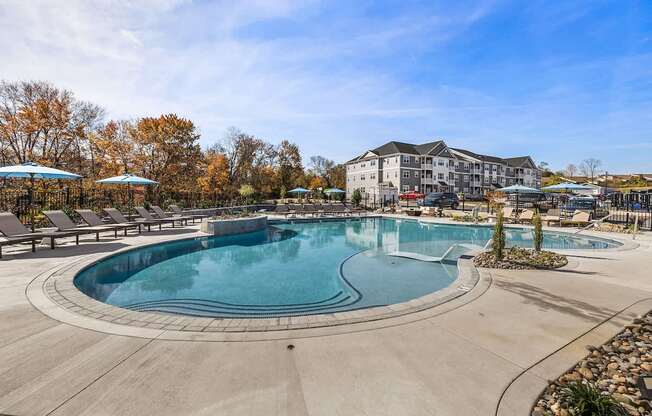 A large outdoor swimming pool surrounded by trees and a building in the background.