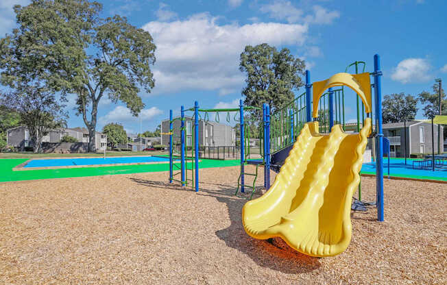 A playground with a yellow slide and a blue and green play structure at Maplewood apartments in Shreveport, LA.