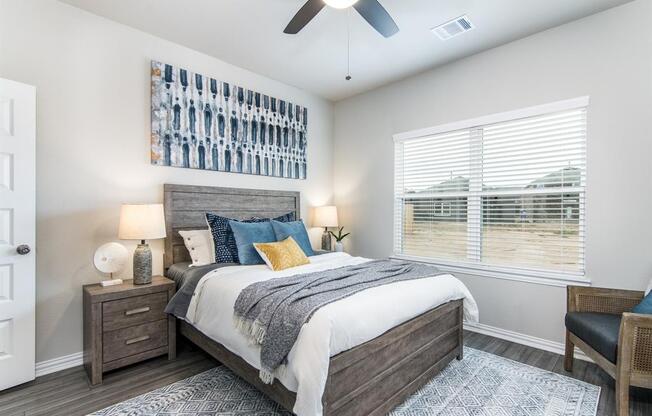 Four-BR Homes for Rent in Katy, TX - Villas at Sunterra - Bedroom with a Large Window, a Ceiling Fan, a Large Bed, Two Nightstands with Lamps, Wood-Style Flooring, and Stylish Decor