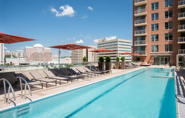 a swimming pool with lounge chairs and umbrellas next to a tall building at The Acadia at Metropolitan Park, Arlington, VA