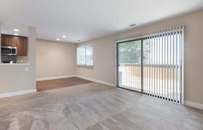 an empty living room with a large sliding glass door to a kitchen