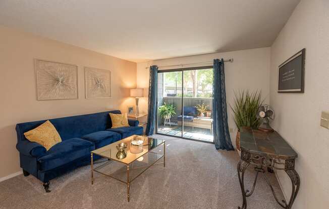 A living room with a blue couch, a glass coffee table, and a plant at Bishop's Court Apartments, California, 95670