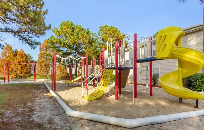 Playground jungle gym and playground slides in a bed of mulch with trees, and swings in the background
