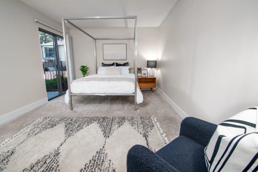 Model apartment bedroom with a bed, chair and rug, and patio door