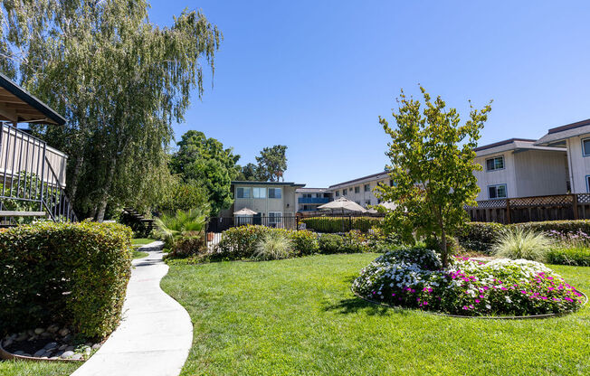 a yard with grass and flowers in front of apartment buildings