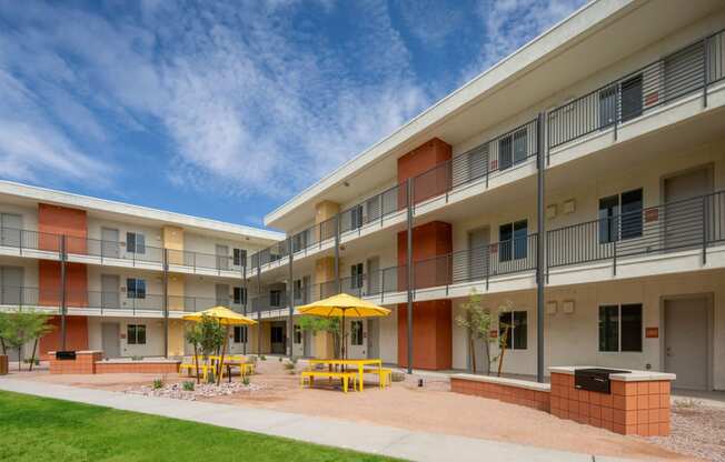 a courtyard with yellow tables and yellow umbrellas in front of an apartment building