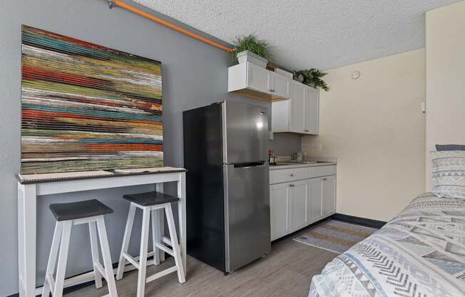 A kitchen area with a refrigerator, bar stools, and a painting on the wall.