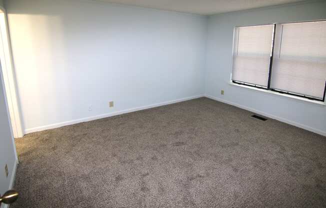 A room with a carpeted floor and a window with blinds.