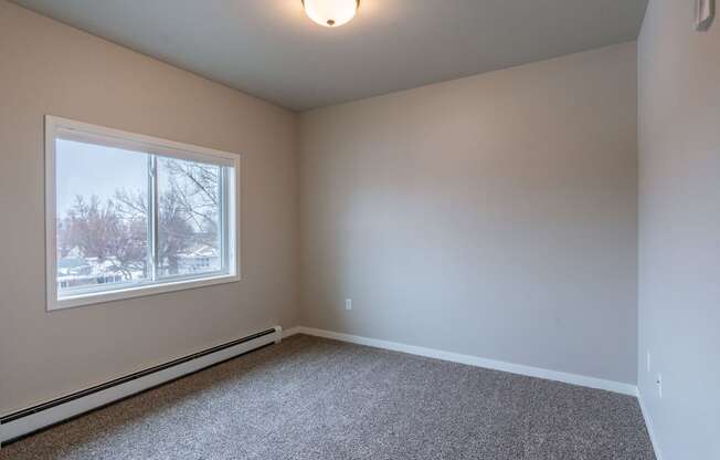 an empty room with carpet and a window. Fargo, ND Prairiewood Meadows Apartments