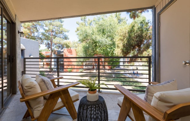 a balcony with two wooden chairs and a table with a plant on it