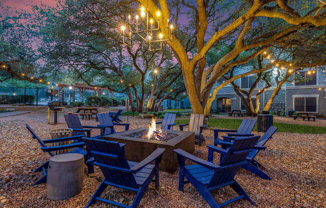 A fire pit surrounded by blue chairs in a gravel area.