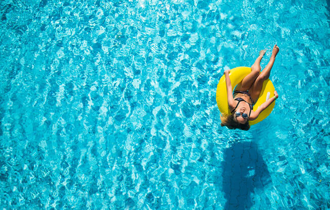 A woman in a yellow swim ring is floating in a pool.