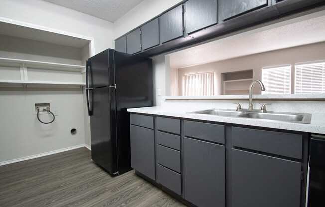 a kitchen with black cabinets and a sink and a refrigerator at The Broadwater at Salado Creek, San Antonio, TX