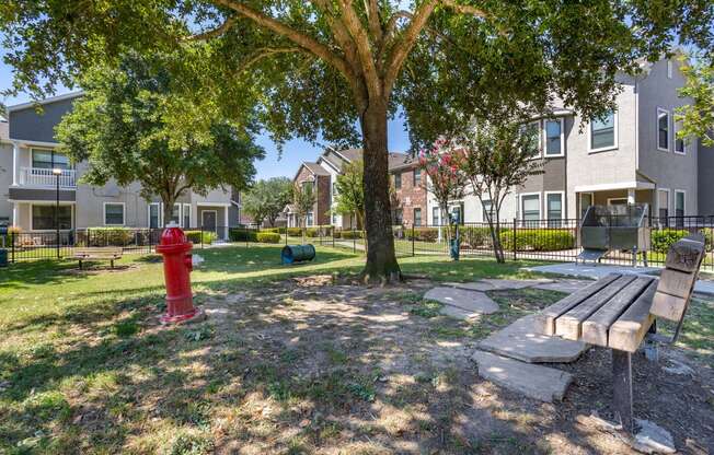 a park with a red fire hydrant and benches in front of an apartment building at Sladestone Shadow Creek, Texas