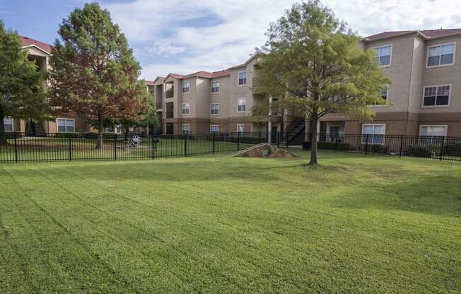 a grassy area with trees in front of an apartment building