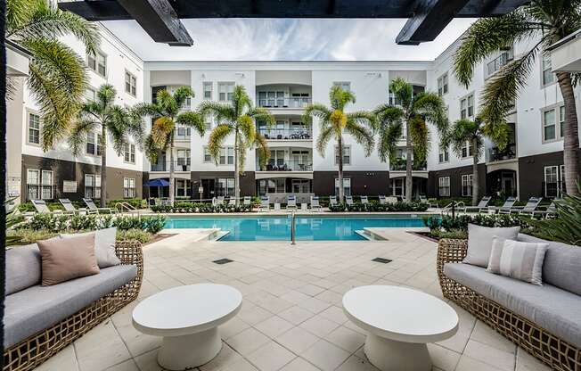 A pool surrounded by palm trees and white furniture.