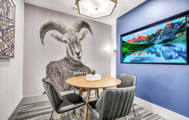 A room with a table, chairs, and a large screen displaying a mountain landscape.